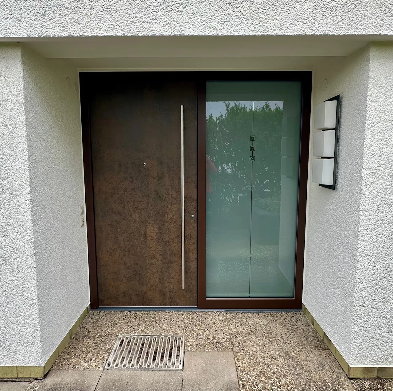 Moderne Haustür mit Seitenteil für die Sanierung Moderne braune Haustür mit langem Edelstahlgriff und verglastem Seitenteil